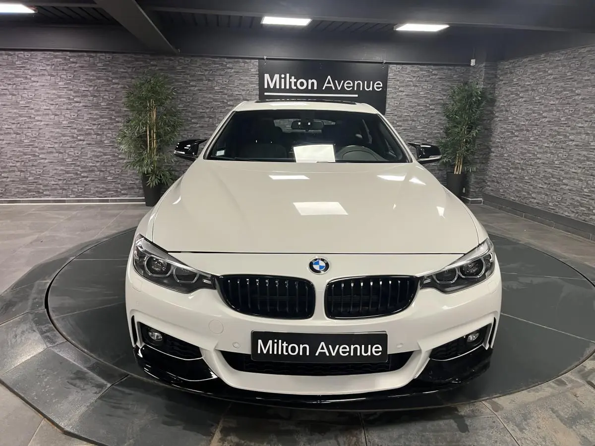 Vue avant d'une BMW Série 4 Gran Coupé blanche avec calandre noire et détails noirs brillants au sol showroom.