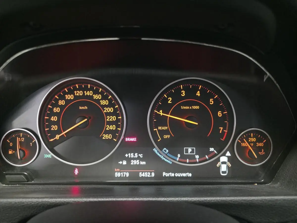 Gros plan sur le tableau de bord numérique de la BMW Série 4 blanc, affichant vitesse, régime moteur et alertes.