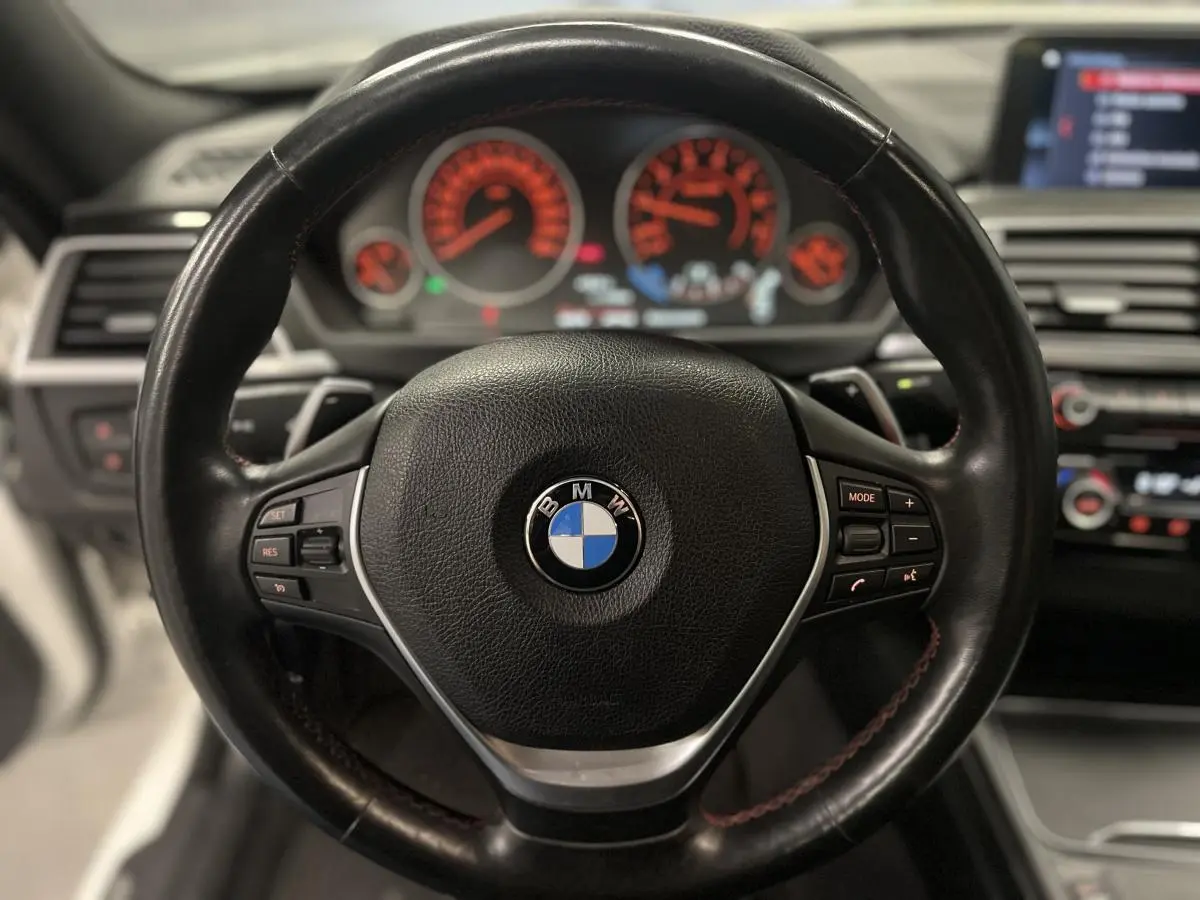 Vue rapprochée du volant cuir noir multifonctions d'une BMW Série 4 430i Gran Coupé, avec tableau de bord éclairé en arrière-plan.