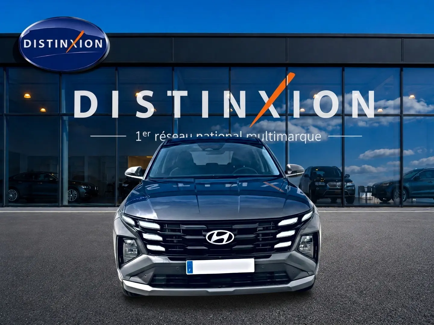 Vue frontale d'un Hyundai Tucson gris ecotronique garé devant une vitrine avec logo Distinxion.