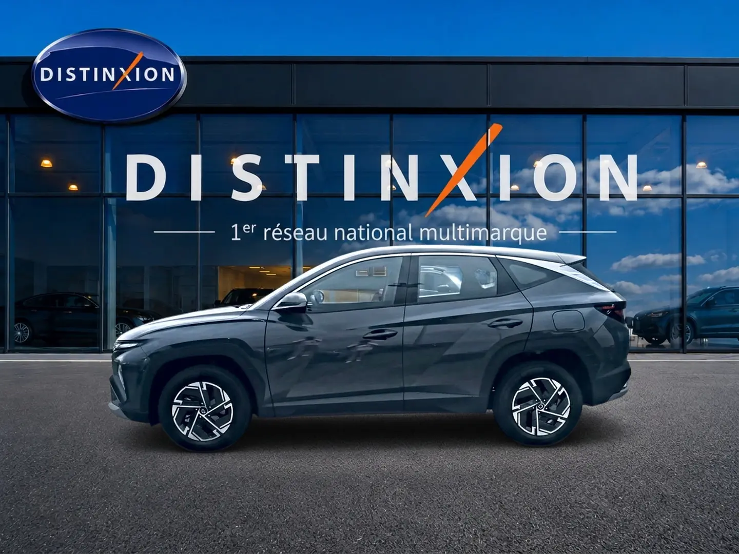 Vue de profil côté gauche du Hyundai Tucson 1.6 t-gdi 239 hybride gris ecotronique devant une vitrine Distinxion.