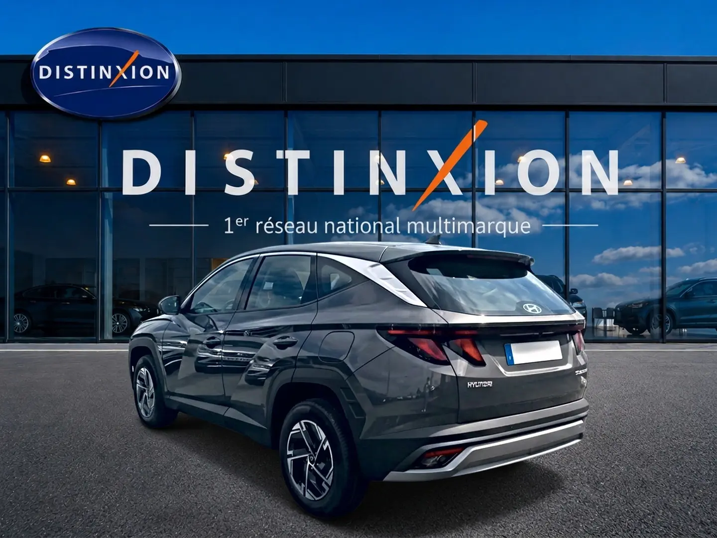Vue 3/4 arrière droite d'un Hyundai Tucson gris ecotronique avec jantes alliage et feux arrière LED, devant une vitrine Distinxion.