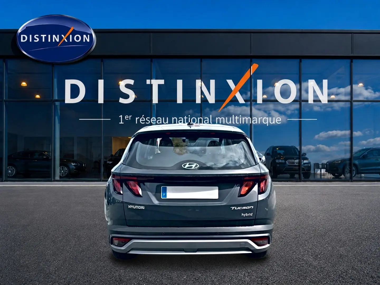 Vue arrière d’un Hyundai Tucson hybride gris écotronique garé devant une vitrine Distinxion avec logo visible.