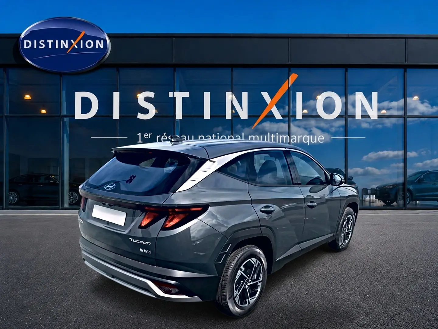 Vue 3/4 arrière droite d'un Hyundai Tucson 2026 gris ecotronique avec jantes alliage et vitres teintées devant un showroom Distinxion.