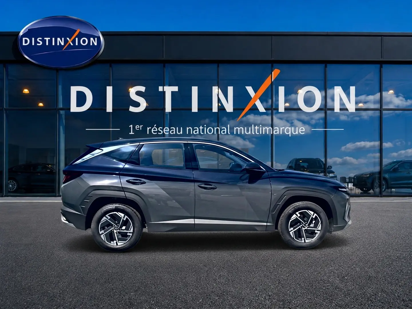 Vue de profil côté gauche du Hyundai Tucson 1.6 t-gdi 239 hybride gris ecotronique devant une vitrine Distinxion.