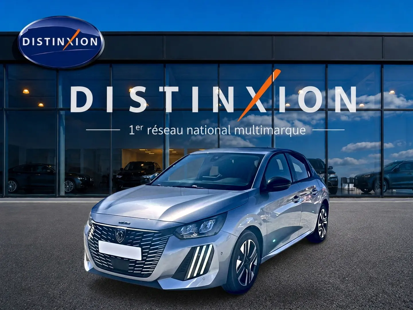 Peugeot 208 1.2 100 Allure gris Artense vue 3/4 avant avec calandre distinctive et jantes alu devant un showroom Distinxion.