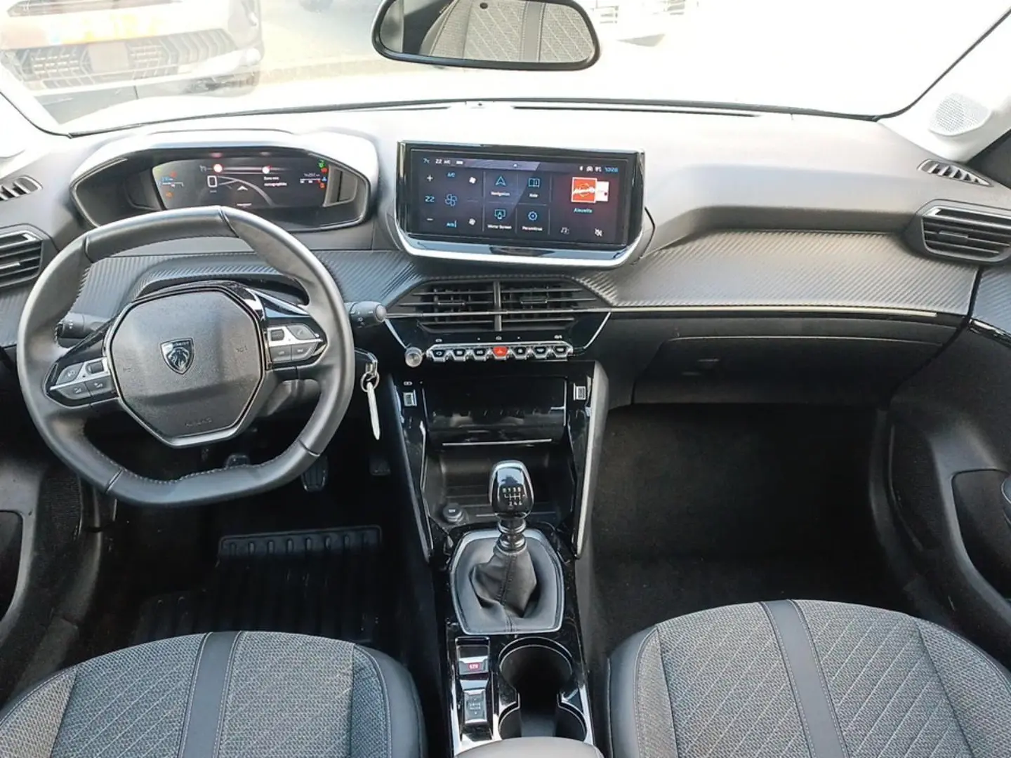 Intérieur avant de la Peugeot 208 1.2 100 Allure 2025, vue du conducteur sur tableau de bord et levier de vitesses manuel.