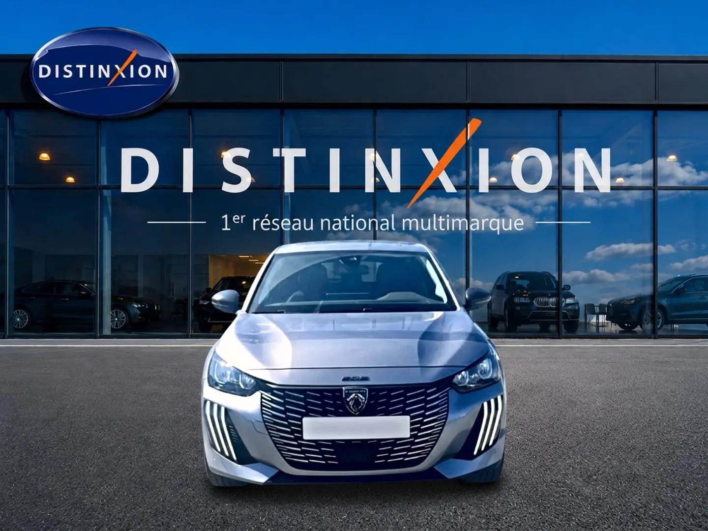 Vue frontale d'une Peugeot 208 1.2 100 Allure gris Artense devant une vitrine avec logo Distinxion.