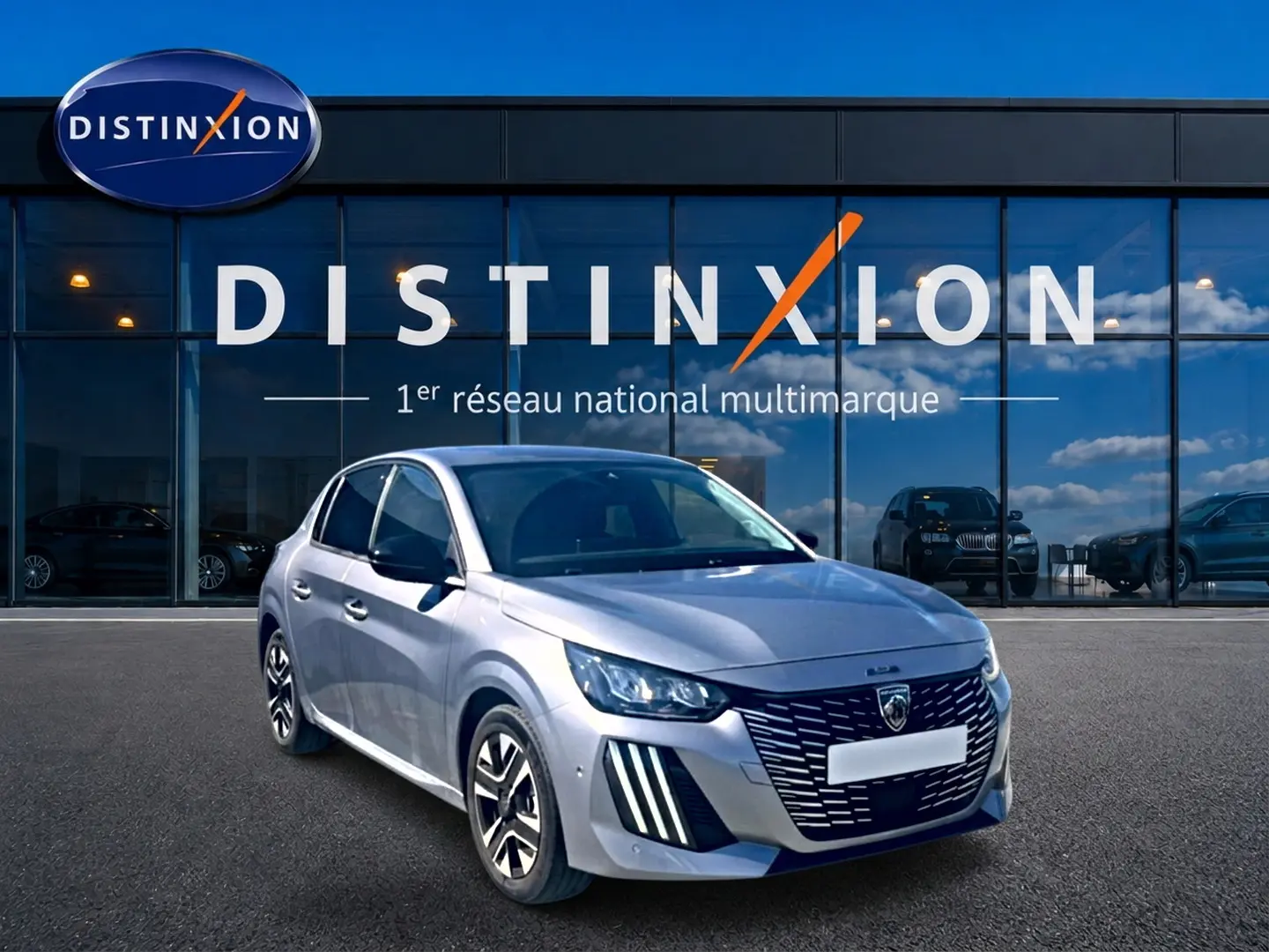 Peugeot 208 gris artense vue 3/4 avant, avec calandre distinctive et jantes alu devant un showroom Distinxion.