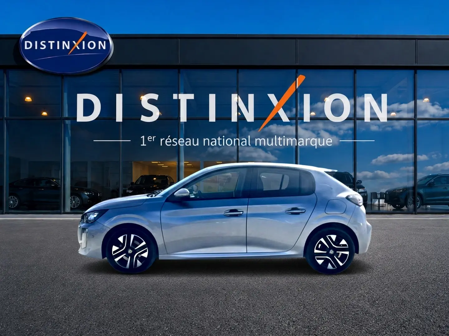 Profil côté gauche de la Peugeot 208 1.2 100 Allure gris Artense, avec jantes alliage et vitres teintées, devant une vitrine Distinxion.