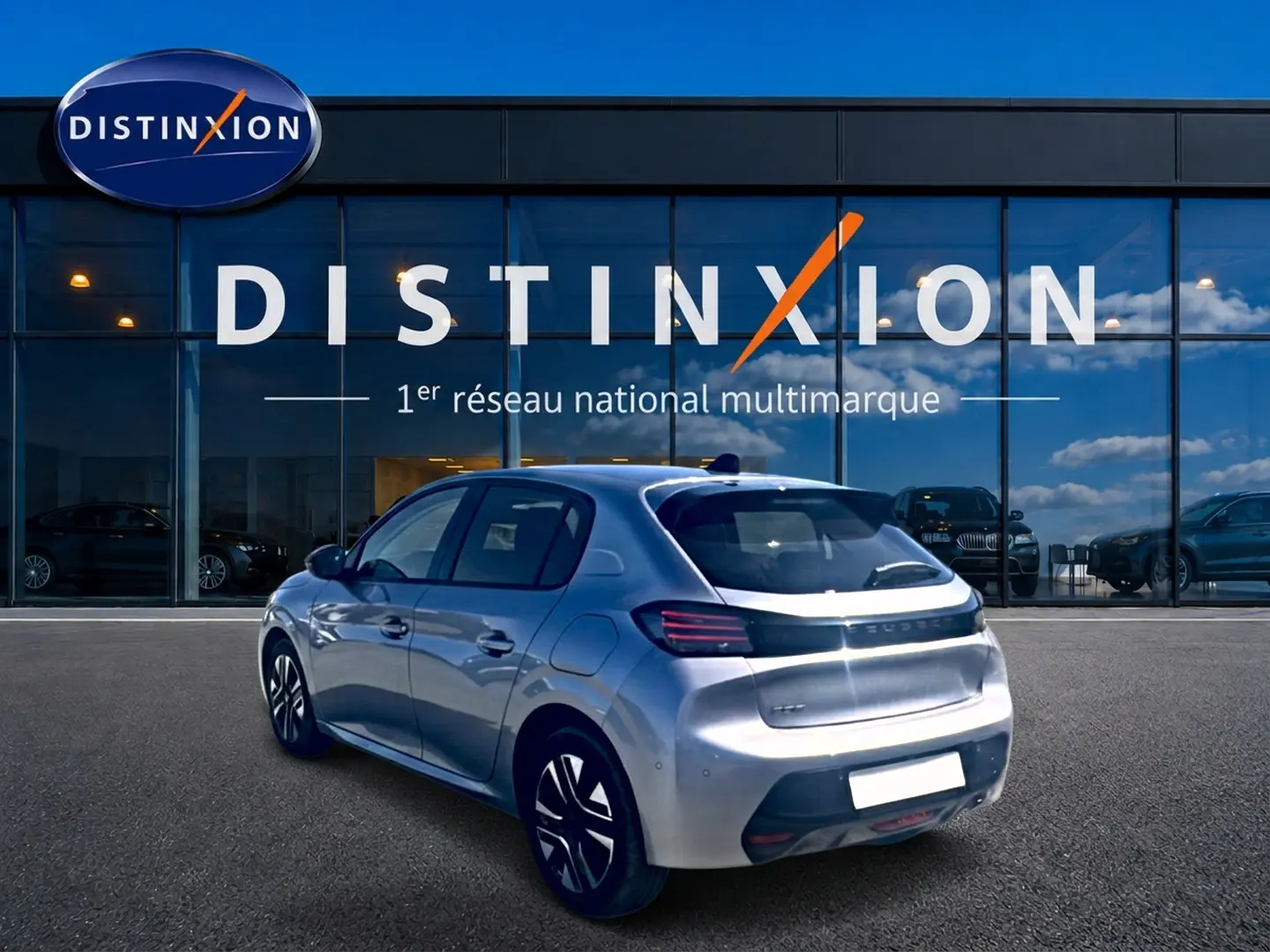 Peugeot 208 1.2 100 Allure gris Artense vue 3/4 arrière droit avec jantes alu devant un showroom Distinxion.