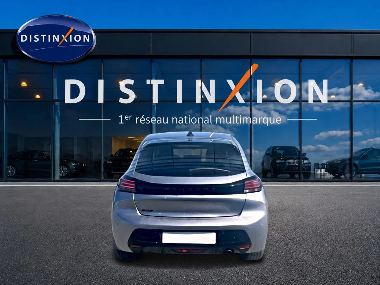 Vue arrière d'une Peugeot 208 gris artense 2025, garée devant une vitrine avec logo Distinxion en arrière-plan.
