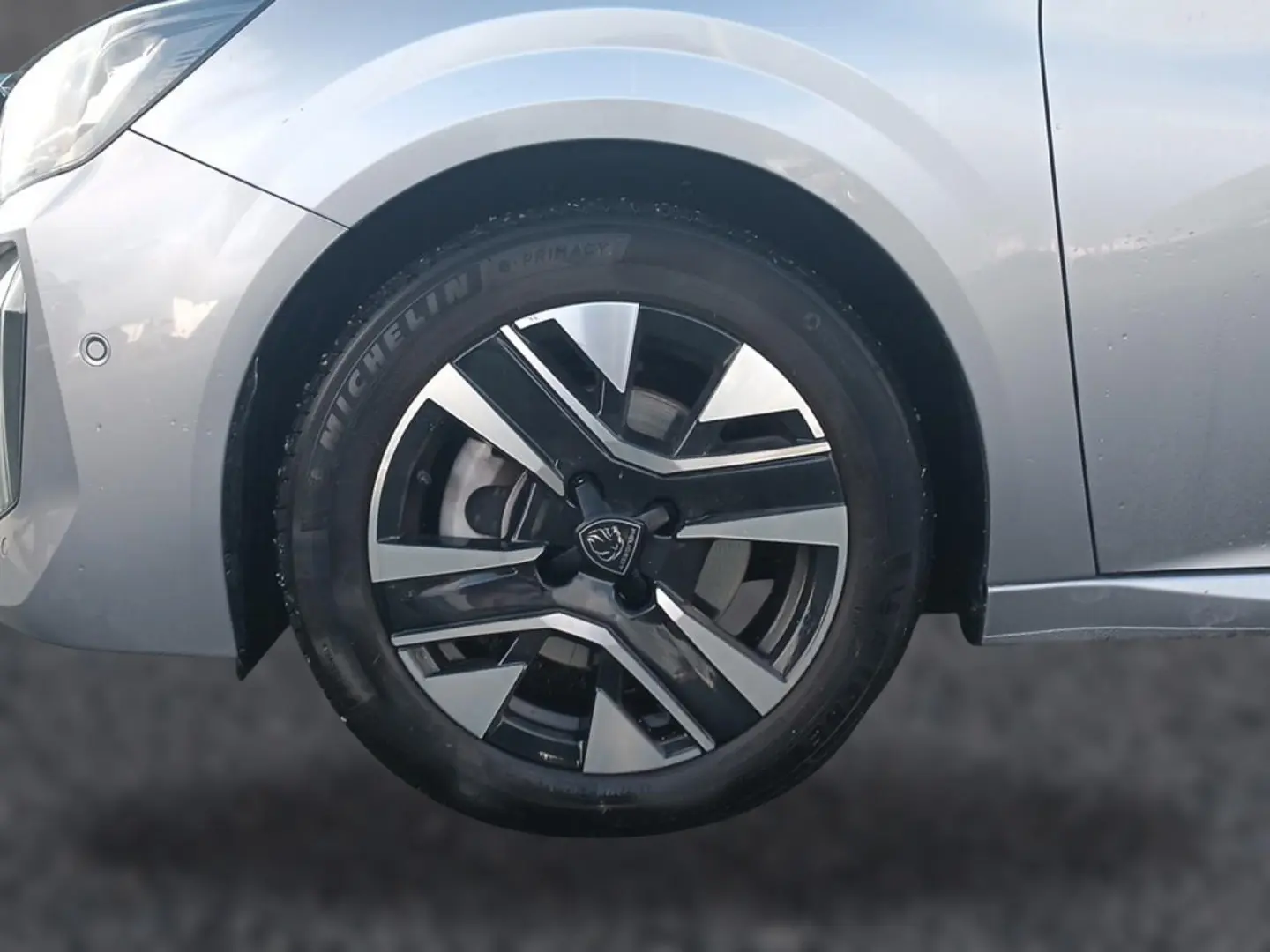 Gros plan sur la roue avant gauche de la Peugeot 208 gris artense avec jante alu bicolore et partie avant du véhicule visible.