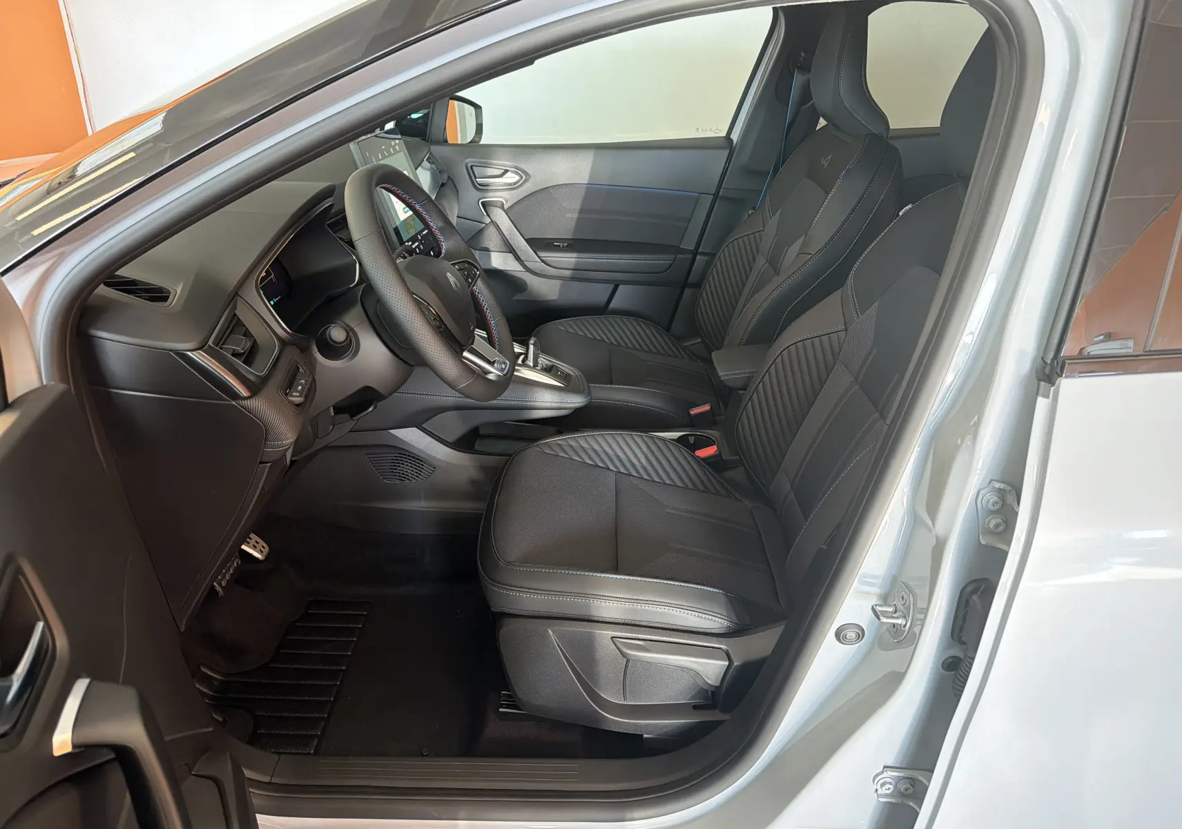 Vue intérieure côté conducteur du Renault Captur E-Tech 160 Esprit Alpine 2026, sièges noirs avec surpiqûres bleues et logo Alpine.