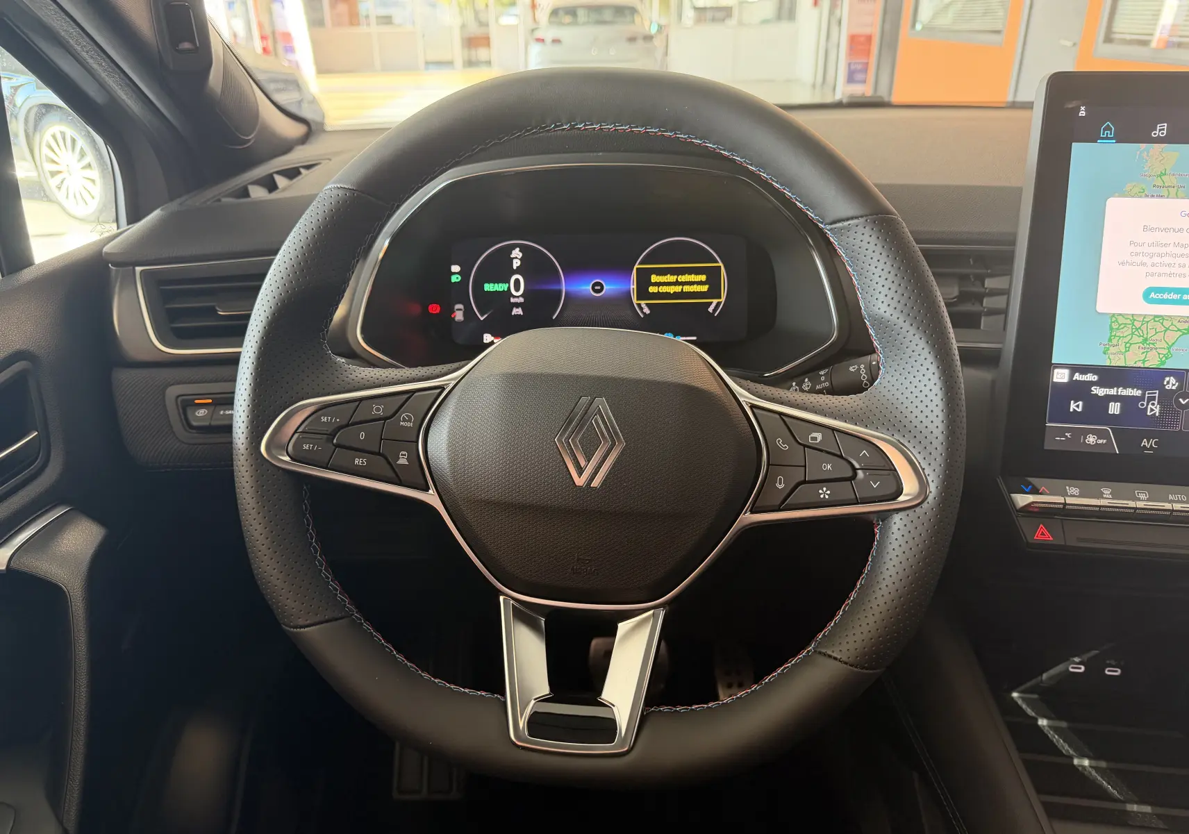 Vue centrée du volant noir perforé avec coutures tricolores et tableau de bord numérique du Renault Captur E-Tech 160 Esprit Alpine.
