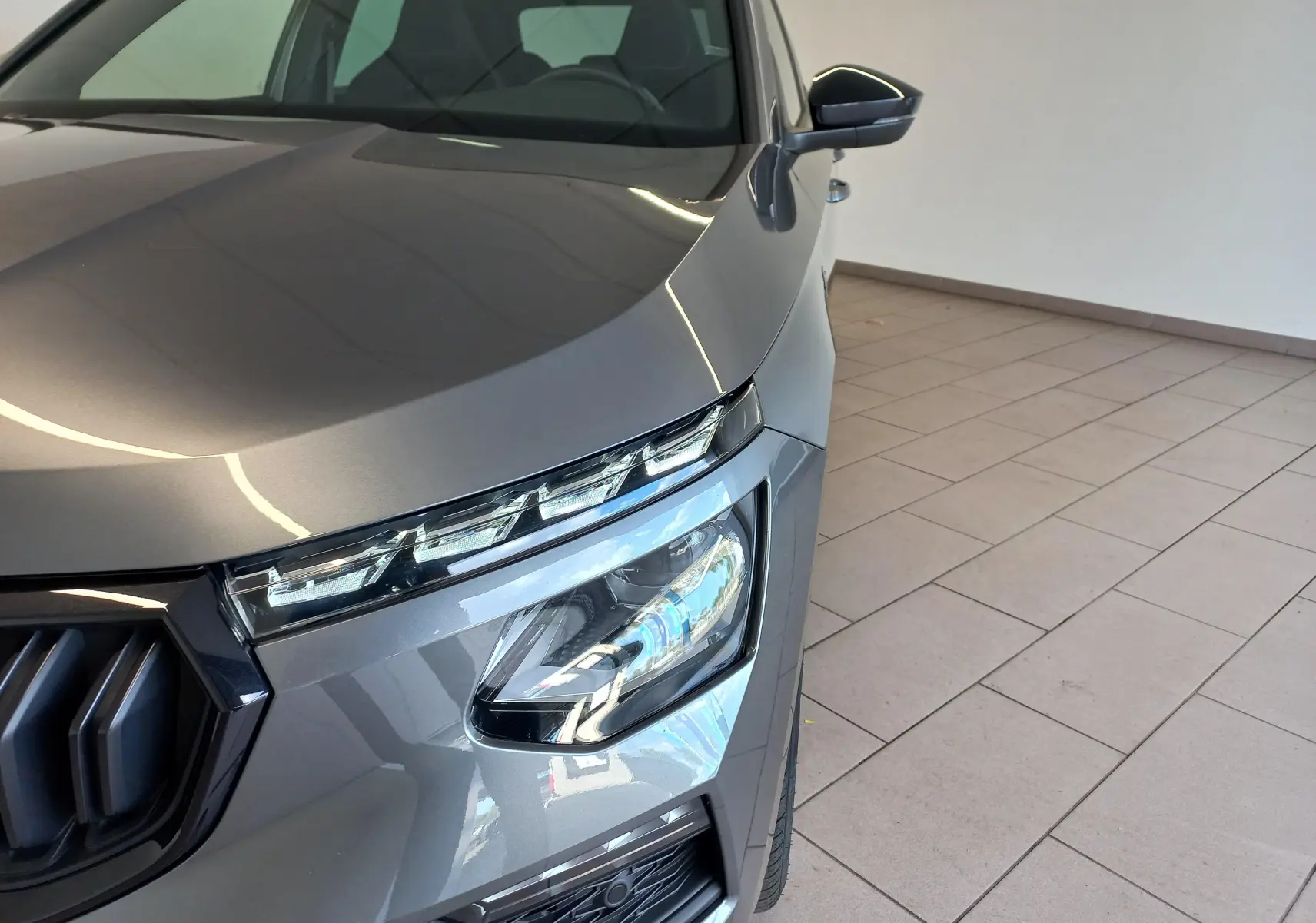 Gros plan sur l’avant droit du Skoda Kamiq Monte Carlo 2024 en gris graphite, mettant en valeur ses phares LED et calandre distinctive.