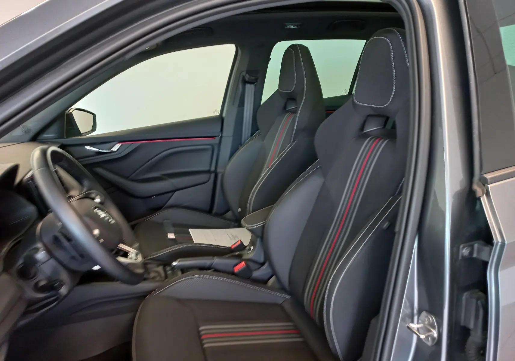 Vue intérieure côté conducteur du Skoda Kamiq 1.5 TSI Monte Carlo gris graphite, sièges sport avec surpiqûres rouges et blanches.