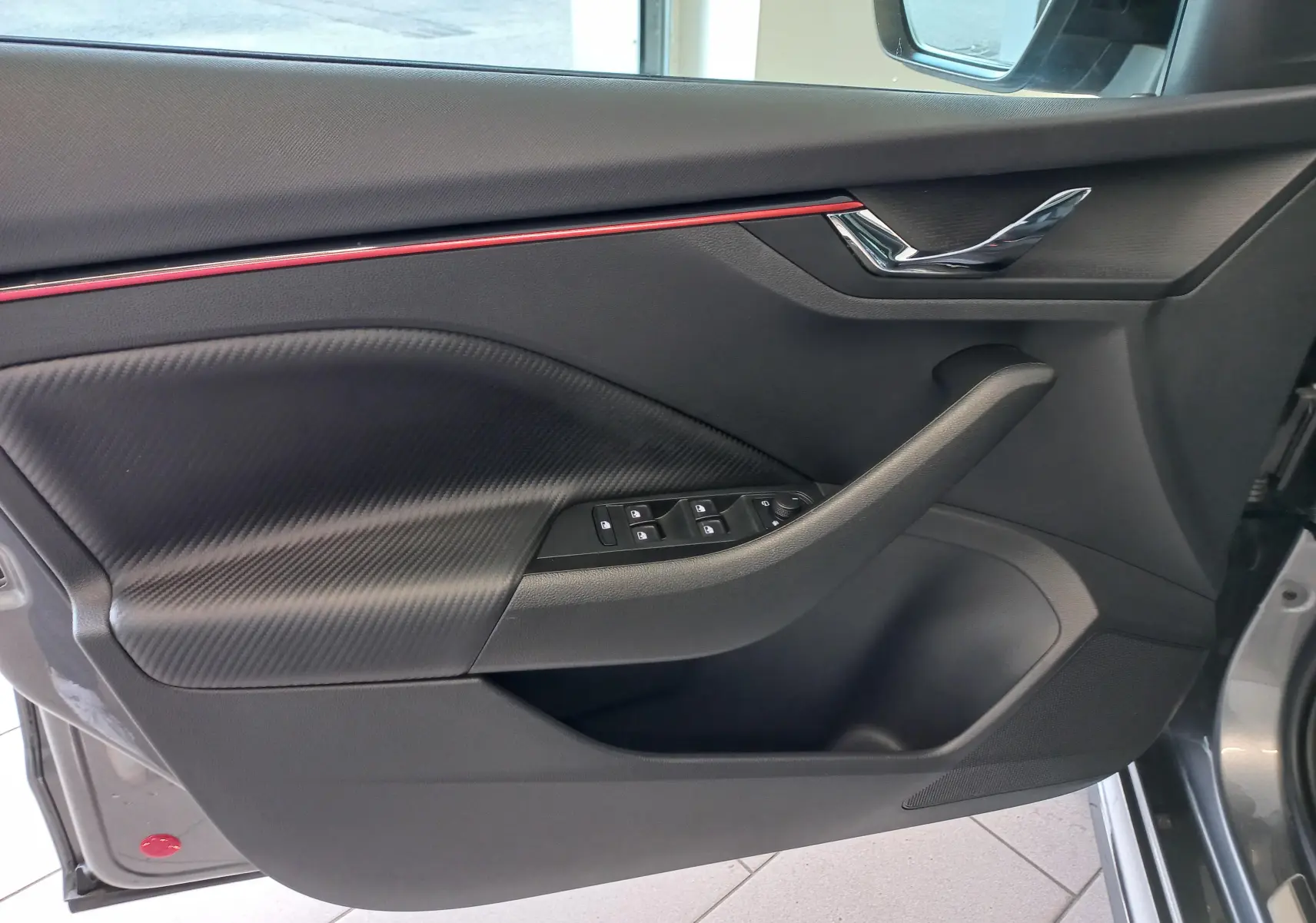 Intérieur côté gauche de la porte Skoda Kamiq Monte Carlo 2024 gris graphite avec insert carbone et bande rouge décorative.