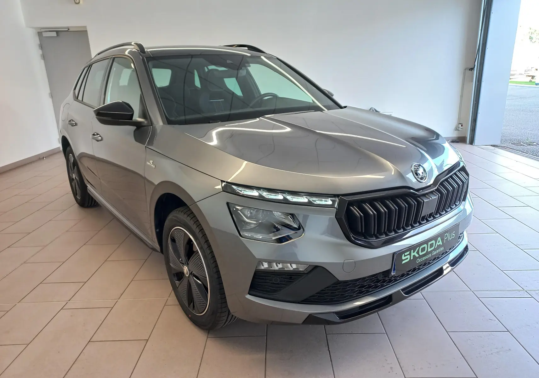 Vue 3/4 avant droite d'un Skoda Kamiq 2024 gris graphite version Monte Carlo avec calandre noire et jantes spécifiques.