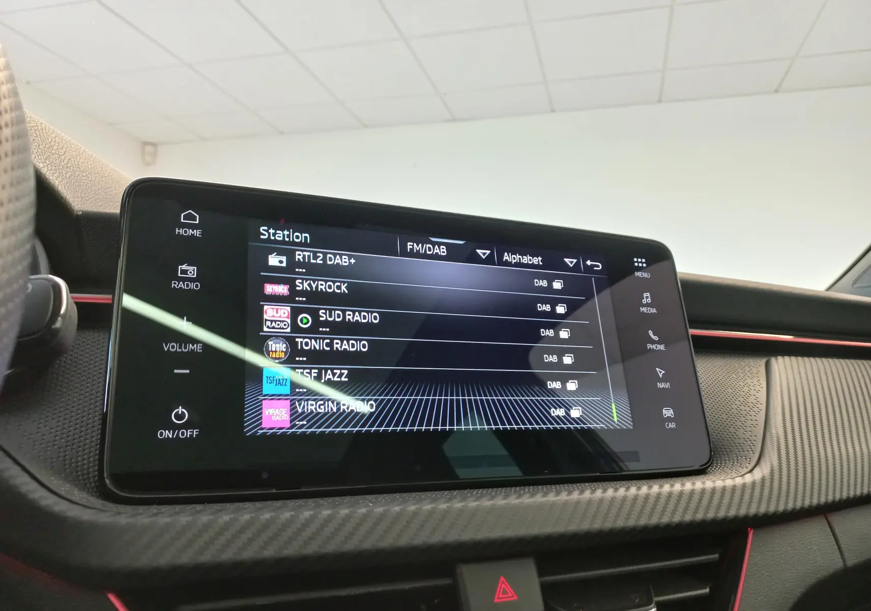Écran tactile central du Skoda Kamiq Monte Carlo 2024 en gros plan, avec finition carbone et bande rouge décorative.
