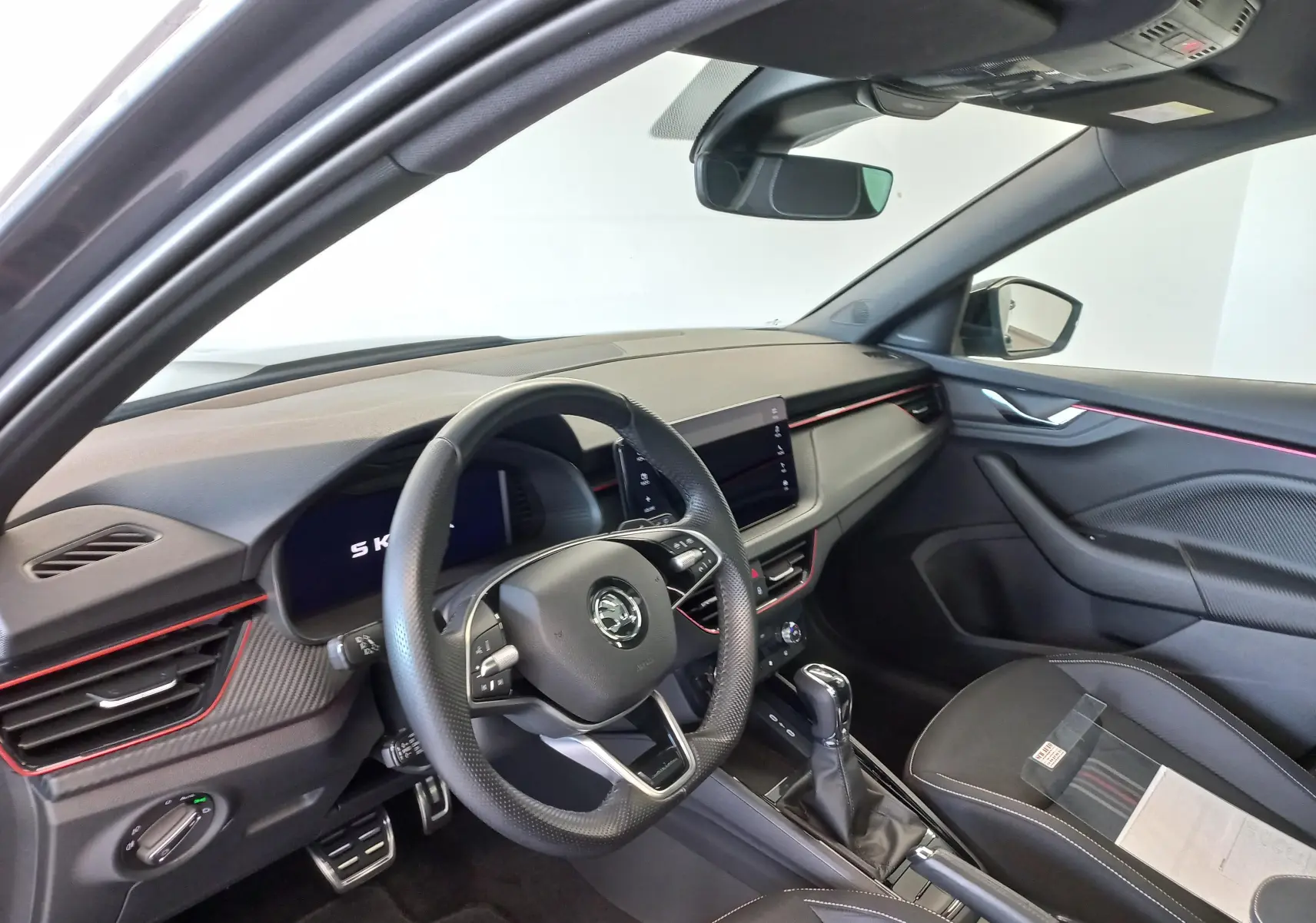 Vue intérieure côté conducteur du Skoda Kamiq 2024 gris graphite, avec éclairage d'ambiance rouge et tableau de bord moderne.