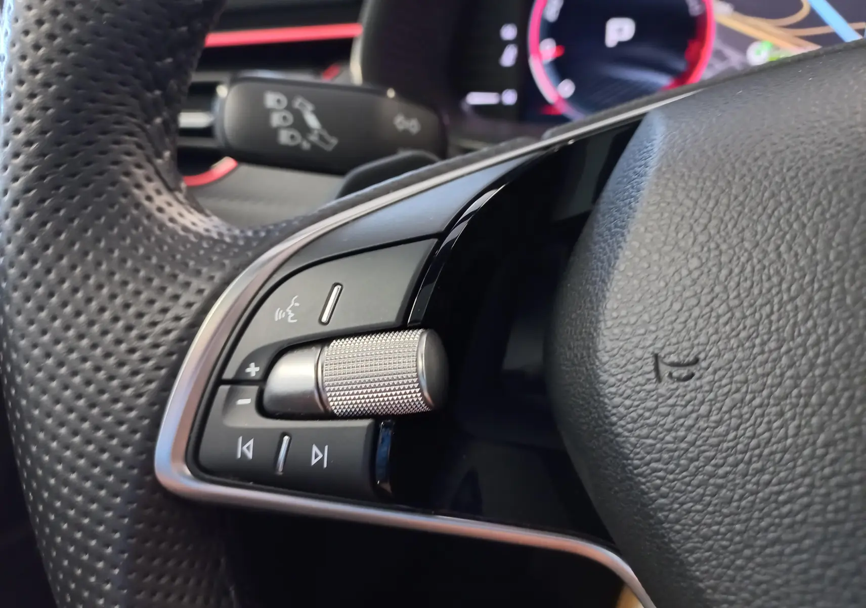 Gros plan sur la partie gauche du volant perforé du Skoda Kamiq 2024 gris graphite, avec commandes audio et molette métallique.
