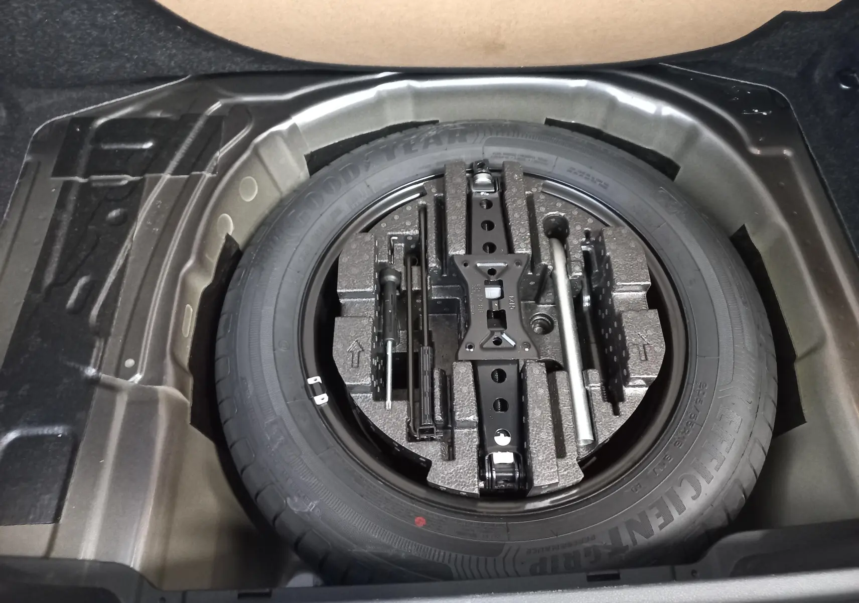 Vue plongeante sur la roue de secours et les outils de bord dans le coffre du Skoda Kamiq 2024 gris graphite Monte Carlo.