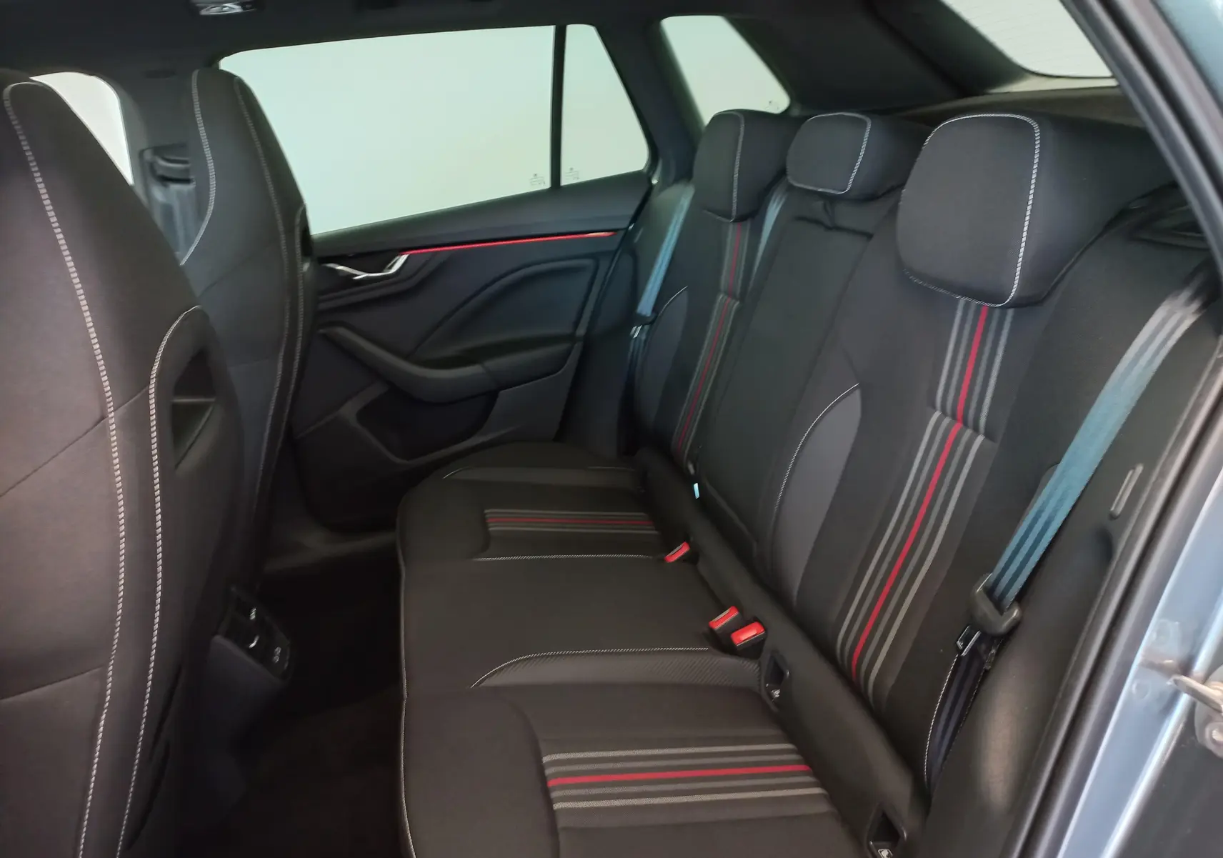 Vue intérieure arrière droite du Skoda Kamiq 2024 Monte Carlo, sièges noirs avec surpiqûres blanches et bandes rouges.