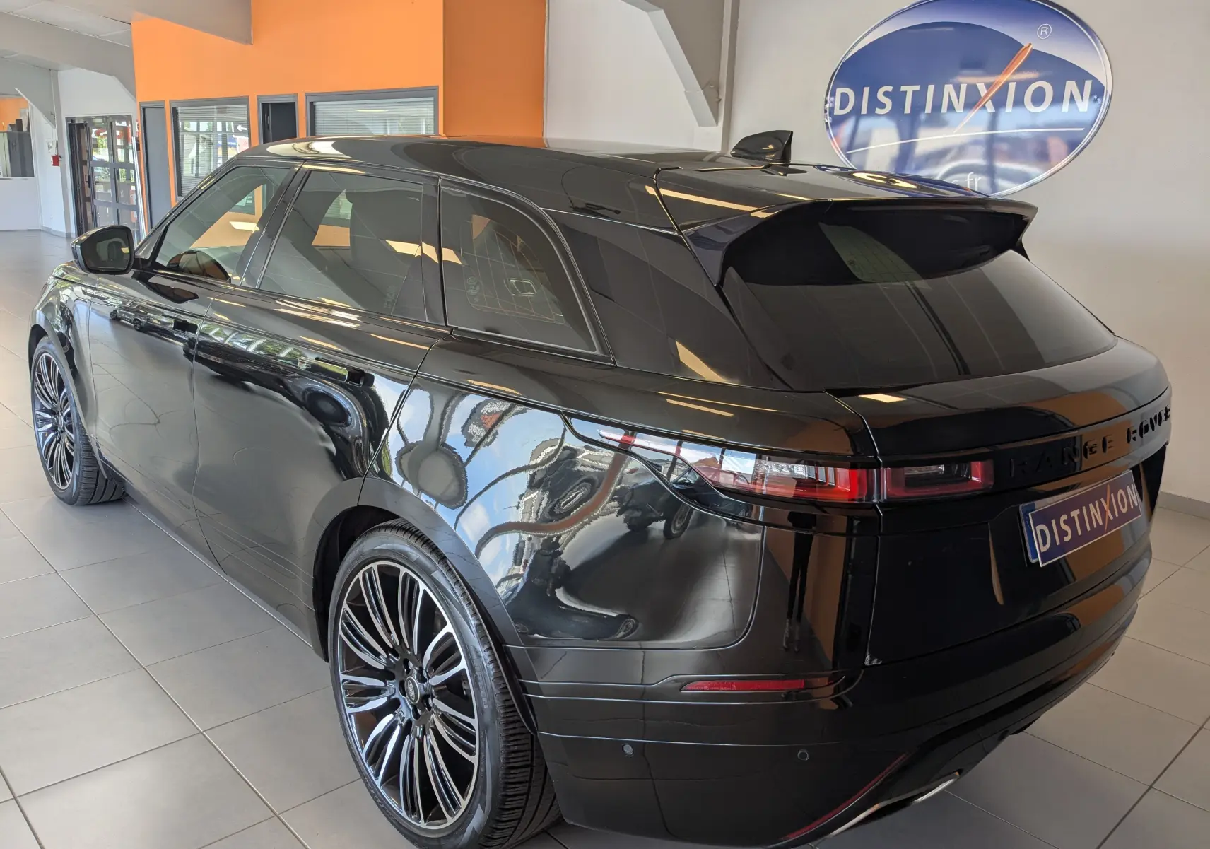 Vue 3/4 arrière droite d'un Range Rover Velar noir brillant avec jantes alliage et vitres teintées en intérieur showroom.