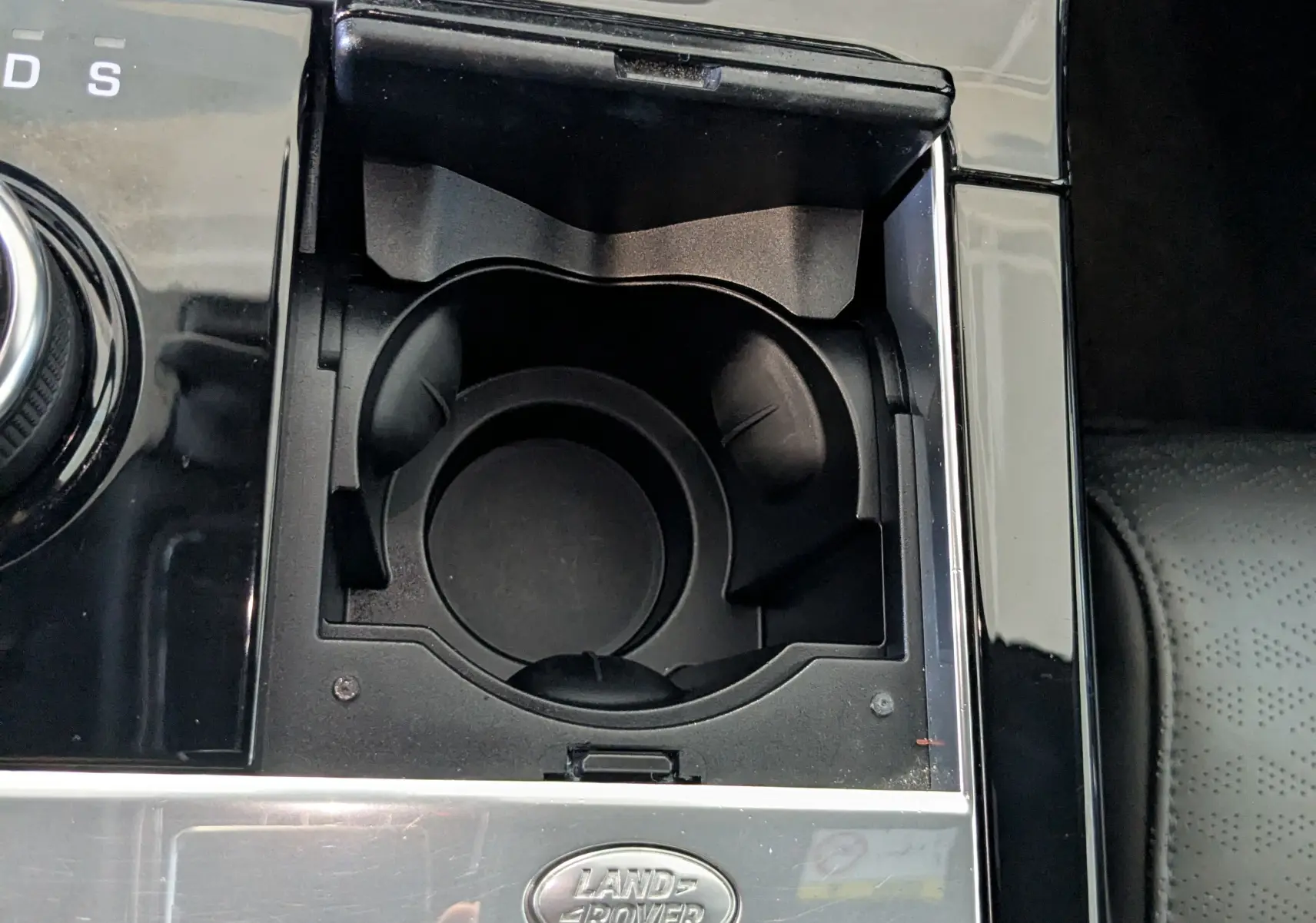 Gros plan sur la console centrale noire du Range Rover Velar 2020 avec porte-gobelets et logo Land Rover argenté.