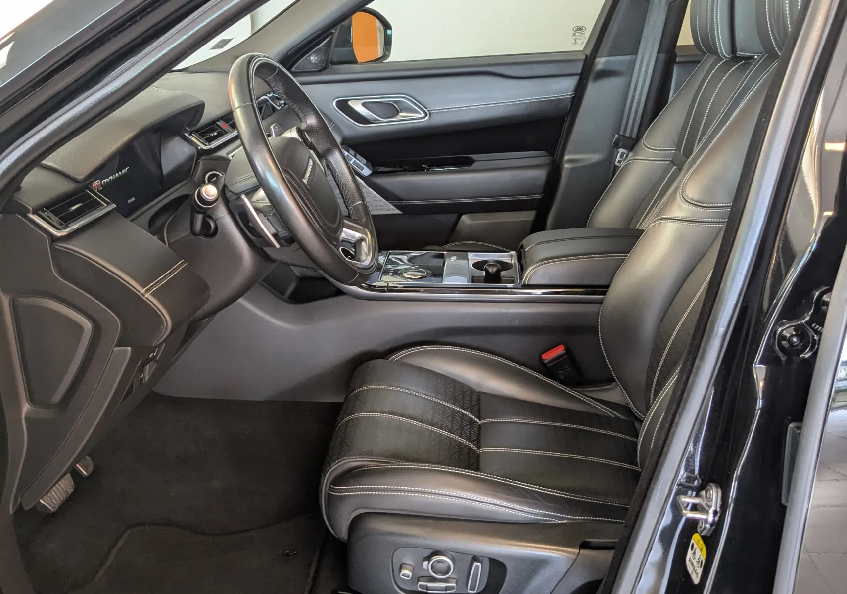 Intérieur côté conducteur du Range Rover Velar noir, sièges cuir noir avec surpiqûres blanches et tableau de bord moderne.