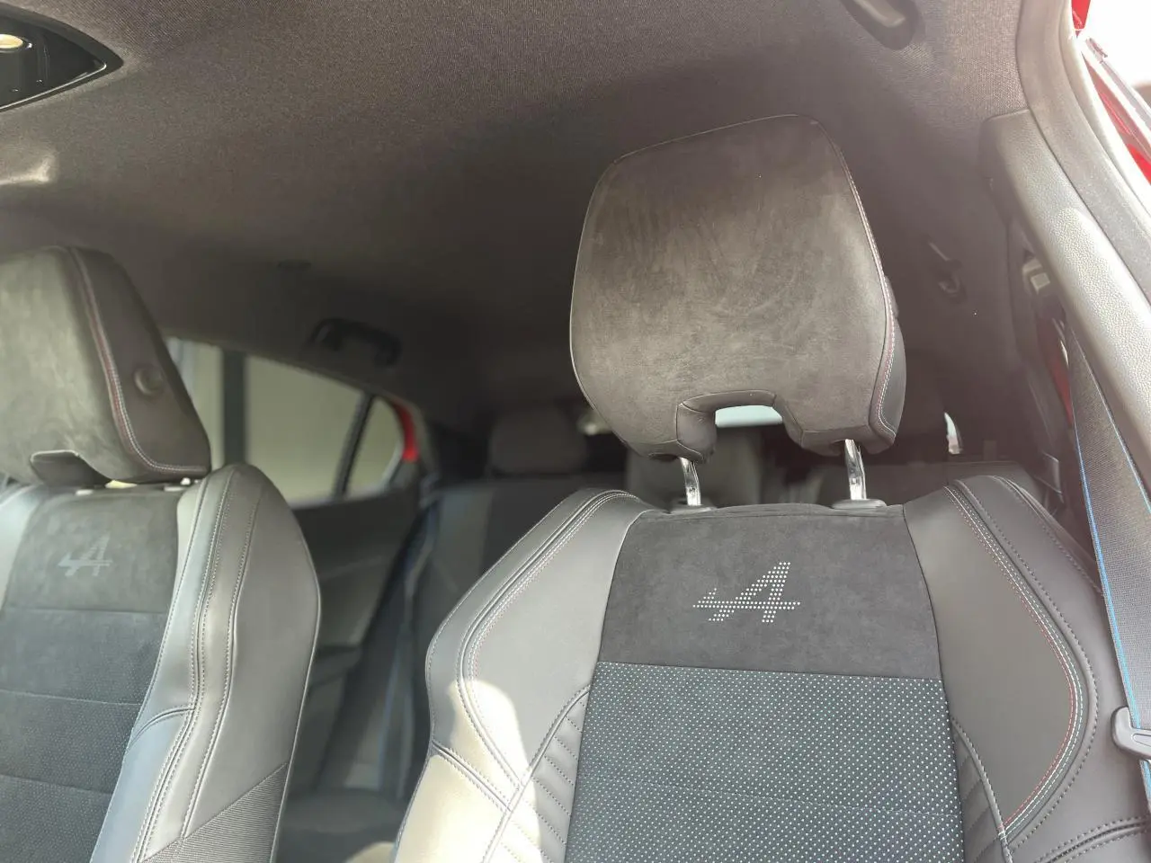 Gros plan sur les sièges avant noirs de la Renault Rafale Esprit Alpine avec logo "A" lumineux et surpiqûres tricolores.