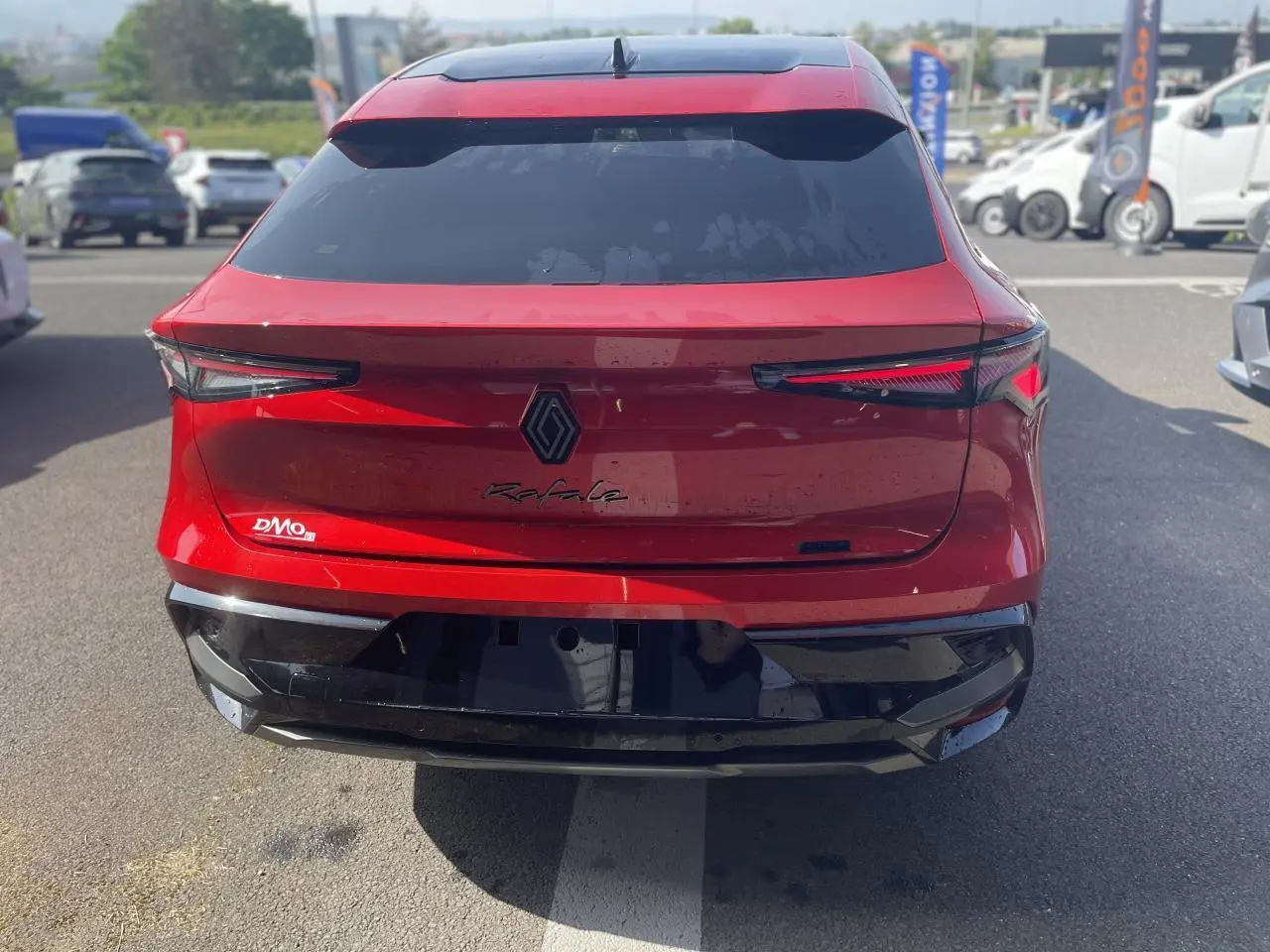 Vue arrière d'une Renault Rafale rouge à toit noir, avec feux arrière LED et logo central noir sur parking.