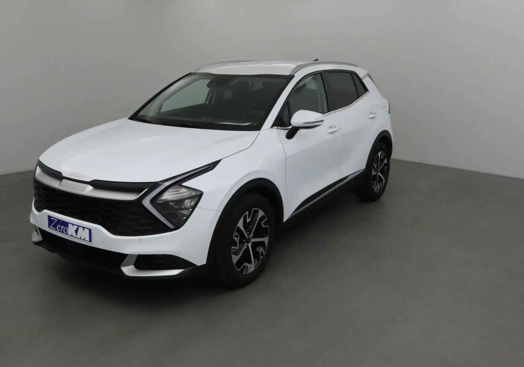 KIA SPORTAGE blanc en 3/4 avant droit, avec calandre noire et jantes alliage bicolores distinctives.