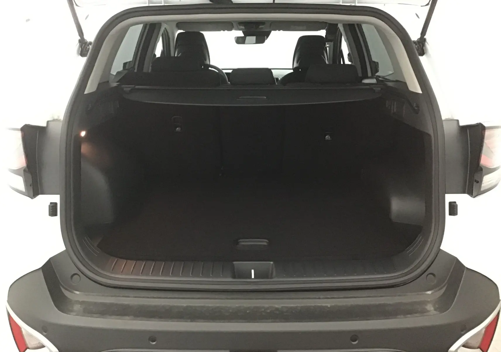 Coffre ouvert d'un KIA SPORTAGE blanc 2025, vue arrière montrant l'espace de chargement et les sièges noirs.