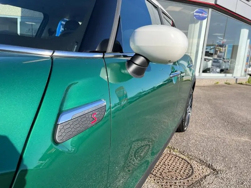 Vue rapprochée du côté gauche d'une MINI Cooper S 2021 en British Racing Green avec rétroviseur blanc et logo S rouge.