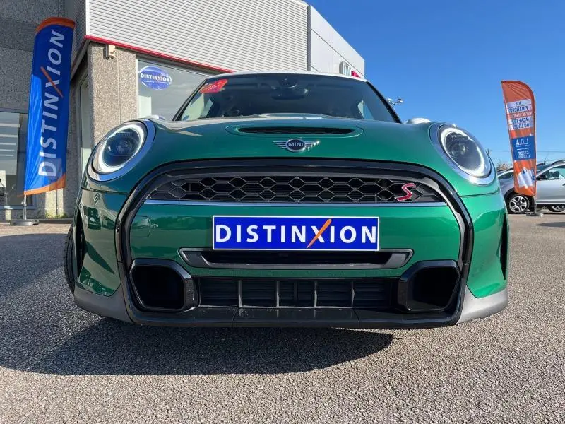 Vue frontale d'une MINI Cooper S British Racing Green avec calandre noire et logo "S" rouge sur parking ensoleillé.