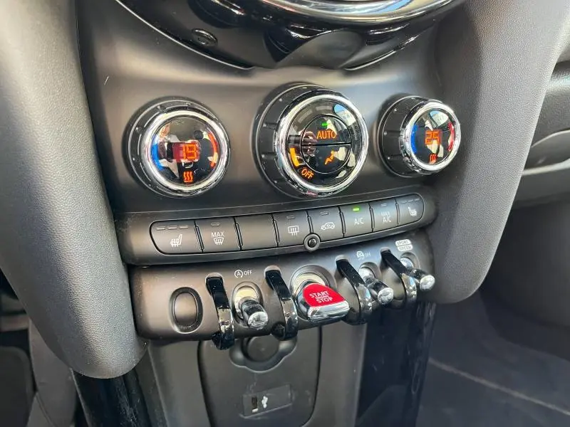 Gros plan sur la console centrale noire de la MINI Cooper S 2021, avec commandes de climatisation et bouton Start/Stop rouge.