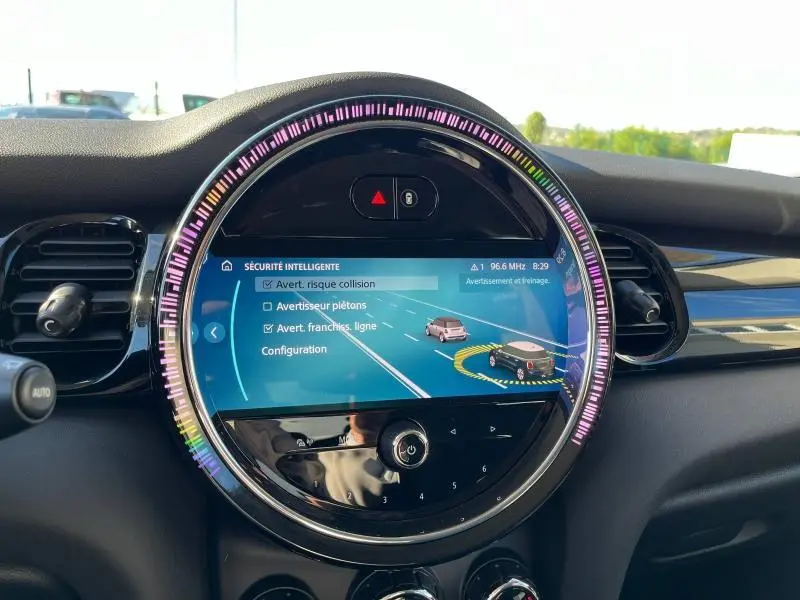 Vue rapprochée du tableau de bord MINI Cooper S 2021 avec écran central rond affichant les alertes de sécurité et éclairage LED coloré.