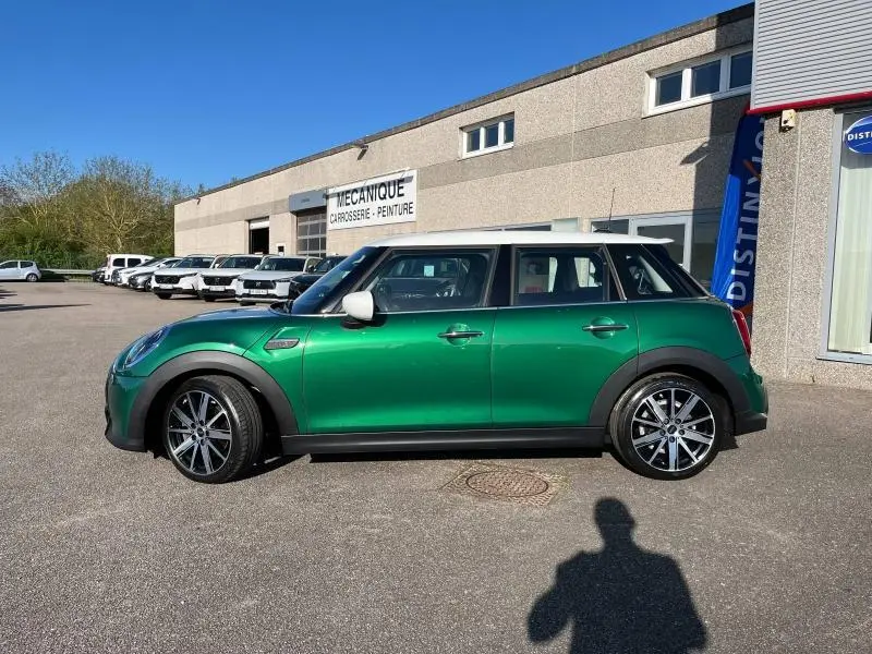 Profil côté gauche d'une MINI Cooper S 2021 British Racing Green avec toit blanc et jantes alliage sur parking.