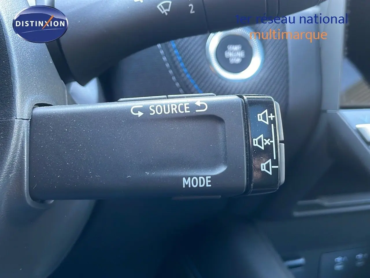 Gros plan sur la commande de source audio et mode du volant du Renault Captur bleu Iron Metal 2025 intérieur noir.