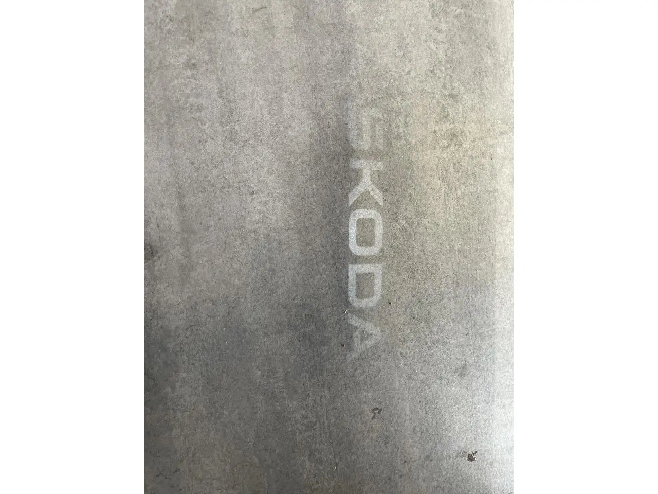 Projection lumineuse du logo SKODA au sol à côté d'une porte de voiture blanche, vue partielle côté droit.