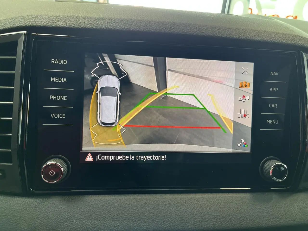 Écran tactile intérieur montrant la caméra de recul et l’aide au stationnement du Skoda Karoq blanc, vue de face.