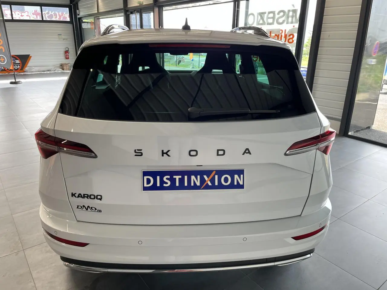 Vue arrière d'un SUV SKODA KAROQ blanc 2025 avec logo SKODA et hayon fermé en intérieur showroom.