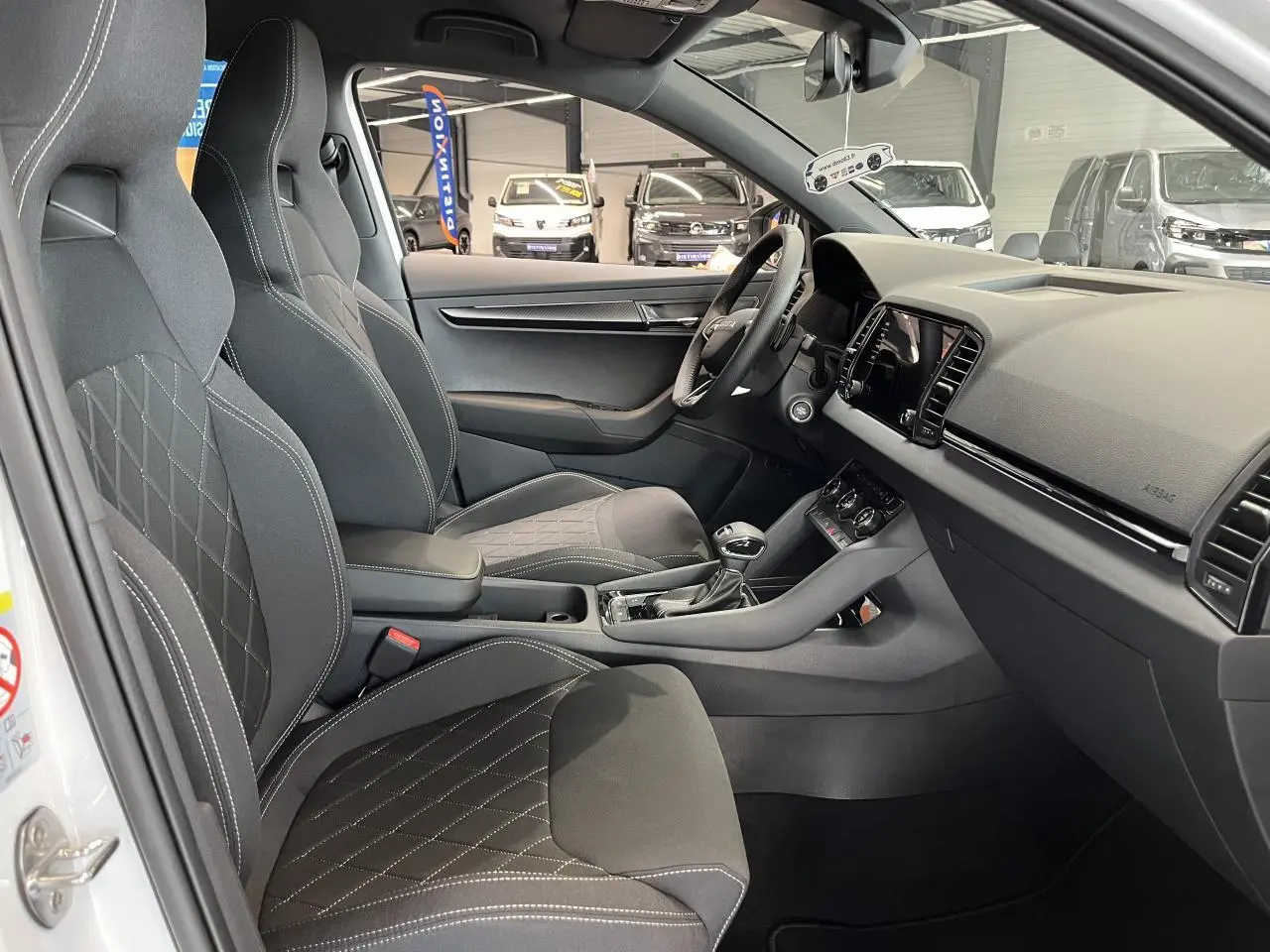 Vue intérieure côté conducteur du Skoda Karoq blanc 2025, sièges sport noirs avec surpiqûres blanches et tableau de bord moderne.