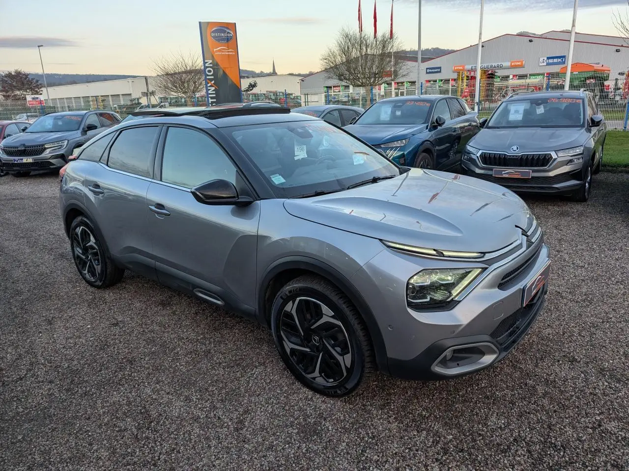 Citroën C4 gris métallisé vue 3/4 avant droit avec jantes alliage noires et toit ouvrant vitré.