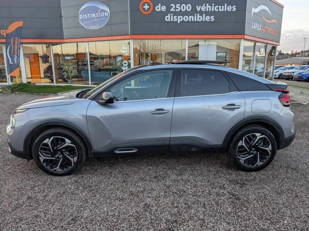 Vue de profil côté gauche d'une Citroën C4 gris métallisé avec jantes alliage et toit ouvrant vitré.