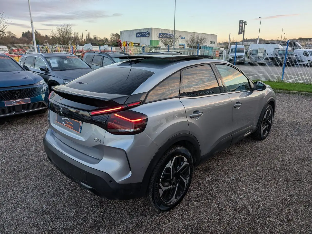 Vue 3/4 arrière droite d'une Citroën C4 gris métallisé avec toit ouvrant vitré et feux arrière LED en V.