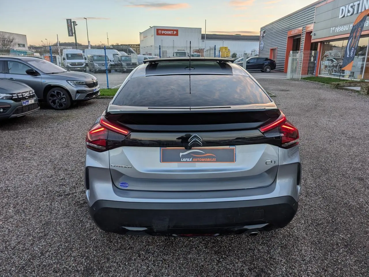 Vue arrière d'une Citroën C4 gris métallisé avec toit ouvrant vitré et feux arrière LED en V allumés.