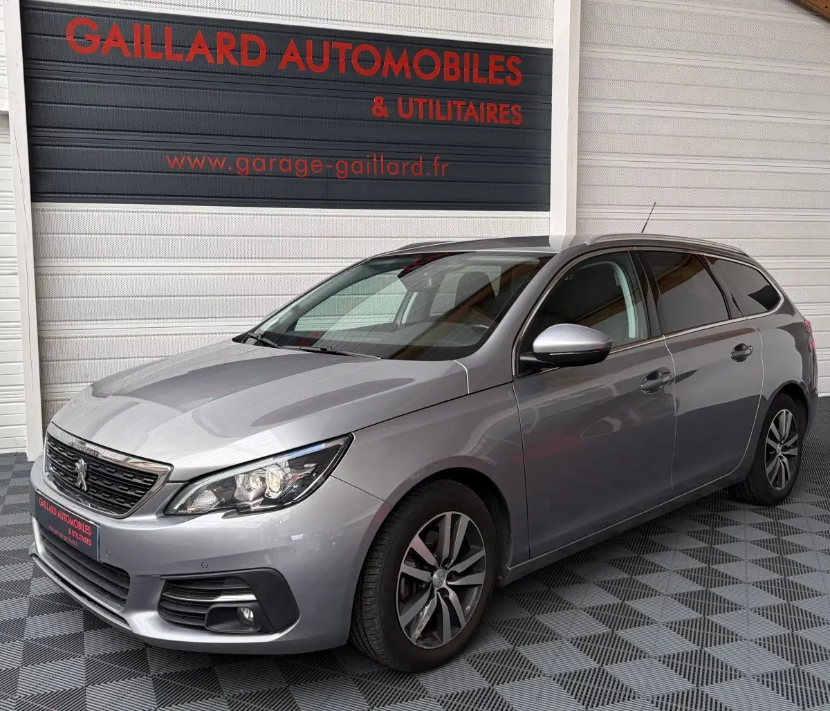 Peugeot 308 BlueHDi 130 S&S Allure gris foncé vue 3/4 avant droit, avec jantes alliage et phares LED allumés.